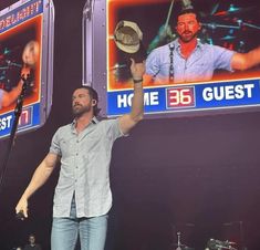 a man standing on top of a stage holding a hat in the air with his right hand