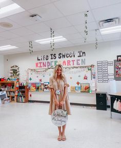 a woman is standing in the middle of a classroom holding a sign that says life is sweet in kindergarttown