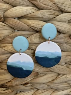 two circular blue and white earrings on top of a woven basket next to each other