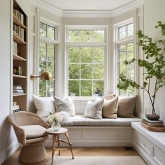 a white window seat with pillows on it and a potted plant in the corner