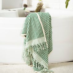 a green and white towel sitting on top of a bath tub next to a plant