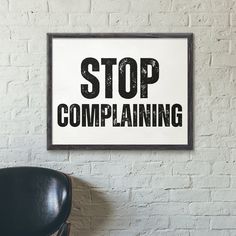 a black chair sitting in front of a white wall with a sign that says stop complaining