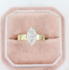 an engagement ring with a pear shaped diamond on it in a pink velvet gift box