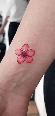 a woman's wrist with a red flower tattoo on the left side of her arm