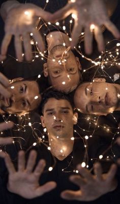 four men are surrounded by string lights in the shape of a circle with their hands