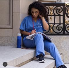 a woman in scrubs sitting on steps reading a book