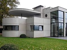 a modern house with an unusual roof and glass windows on the front lawn, surrounded by lush green grass