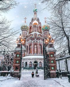 the church is surrounded by trees and snow on the ground, with two people standing in front of it