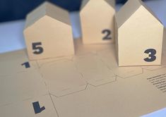 three paper houses sitting on top of a table with numbers cut out to spell them