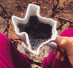 a person holding a white bowl with black liquid in it on top of some rocks