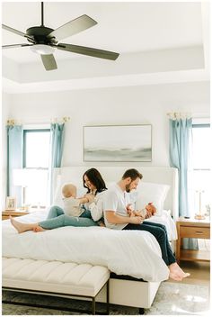 a man and woman are sitting on a bed with their baby in front of them