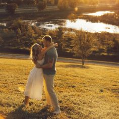 a man and woman embracing each other in a field with the sun setting behind them