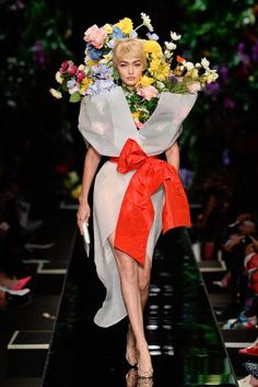 a woman is walking down the runway with flowers in her hair and an orange bow around her neck