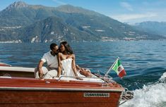 a man and woman sitting on the back of a boat in the water with mountains in the background