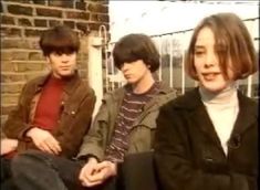 three young men sitting next to each other in front of a brick wall and fence