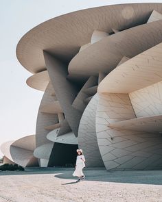 a woman is walking in front of a building that looks like a huge structure with many curves