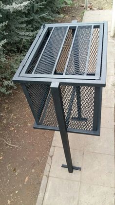 a black metal table sitting on the side of a sidewalk next to a tree and bushes