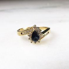 "This is a vintage 14K yellow gold pear sapphire & diamond cocktail ring. The sapphire is 6mm x 4.12mm. There are 19 round diamonds with a total carat weight of .095ct. They have overall G color with I1 clarity. The ring face measures 3/8\" tall x 1/4\" wide. The band is sized at a 7. Total weight of the ring is 3.2grams/2.1dwt. This is a vintage, previously owned ring. Therefore, light wear can be expected. There is no visible damage." Pear-shaped Yellow Gold Sapphire Ring, Pear-shaped Sapphire Ring With Diamond Accents, Yellow Gold Cocktail Ring, The Ring Face, Dark Sapphire, Gold Cocktail, Antique Diamond Rings, Gold Cocktail Ring, Sapphire Diamond Ring