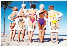 four women in swimsuits standing on the beach with their backs to each other