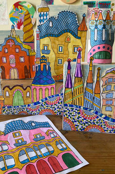 several colorful paper cut outs on a wooden table with artwork in the background, including buildings and kites