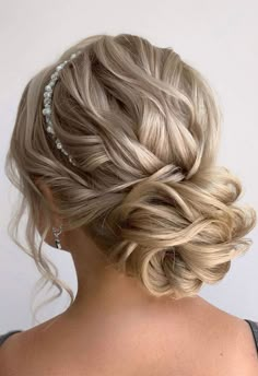 a woman with blonde hair in a low updo and pearls on her head is looking back at the camera