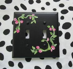 a black light switch cover with pink flowers painted on it and green vines in the middle