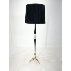 a lamp that is on a table with a black lampshade and a white wall behind it