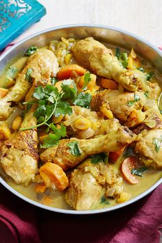 a pan filled with chicken and vegetables on top of a red cloth next to a blue book