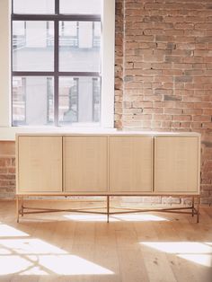 a white cabinet sitting in front of a window next to a wooden floor and brick wall