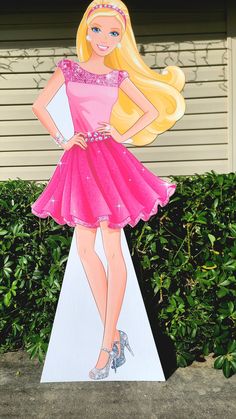 a cardboard cutout of a barbie doll standing on top of a white pedestal in front of bushes