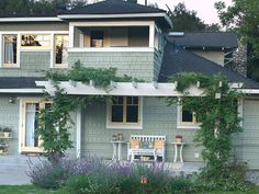 a house with some plants growing on the side of it and a bench in front