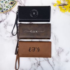 three personalized leather wallets on a marble countertop with flowers in the background