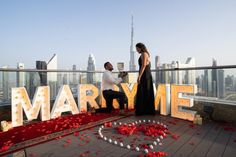 a man kneeling down next to a woman in front of a sign that says marry me