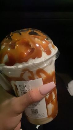 a person holding up a cup filled with ice cream and caramel