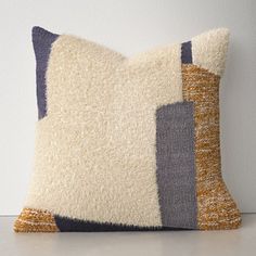 a decorative pillow made out of various colored squares on a white surface with a gray wall in the background