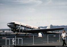 a man walking past an airplane on the tarmac in front of a chain link fence