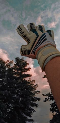 a person wearing gloves is holding their hand up in the air with trees behind them