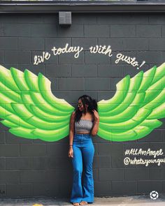 a woman standing in front of a wall with green wings painted on it and the words we today with guse