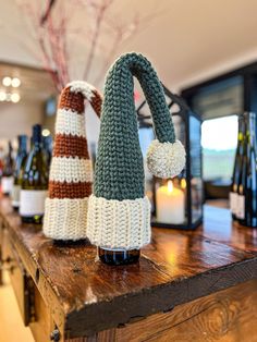 two knitted hats sitting on top of a wooden table next to bottles of wine