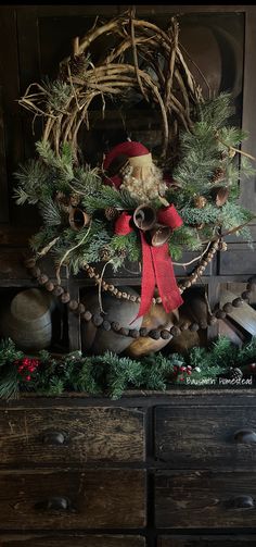 a christmas wreath on top of a dresser with bells and pine cones around it,