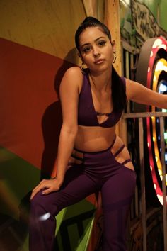 a woman sitting on top of a metal rail next to a colorful wall with neon lights