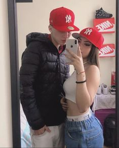 a man and woman taking a selfie in front of a mirror with baseball caps on