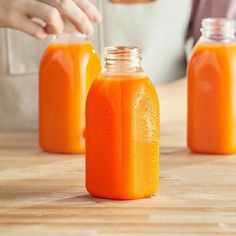 three jars filled with orange liquid sitting on top of a wooden table