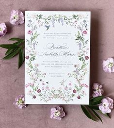 a wedding card with flowers and greenery on it, next to some purple flowers