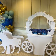 a white horse drawn carriage sitting next to a blue and gold balloon filled wall behind it