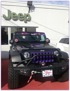 a jeep parked in front of a jeep dealership with purple lettering on the front