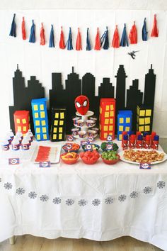 a spiderman themed birthday party with cake and snacks on a table in front of a cityscape backdrop