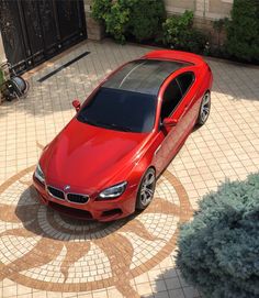 a red car parked in front of a building on top of a brick floored driveway