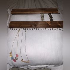 two necklaces are hanging on a wooden hanger next to a white bed sheet