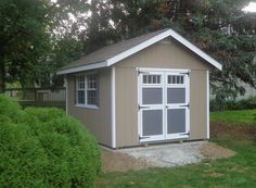 a small shed sitting in the middle of a yard with grass and bushes around it